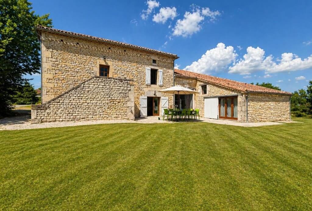 Longue maison en pierre du Quercy et sa pelouse tondue, sous un ciel d'été
