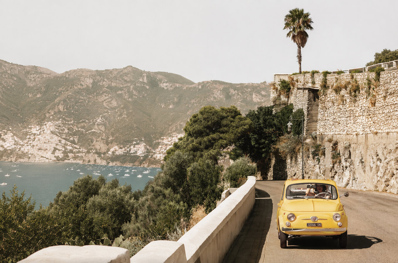 Fiat 500 jaune sur la route en corniche de la côte amalfitaine, la baie de Positano en arrière-plan